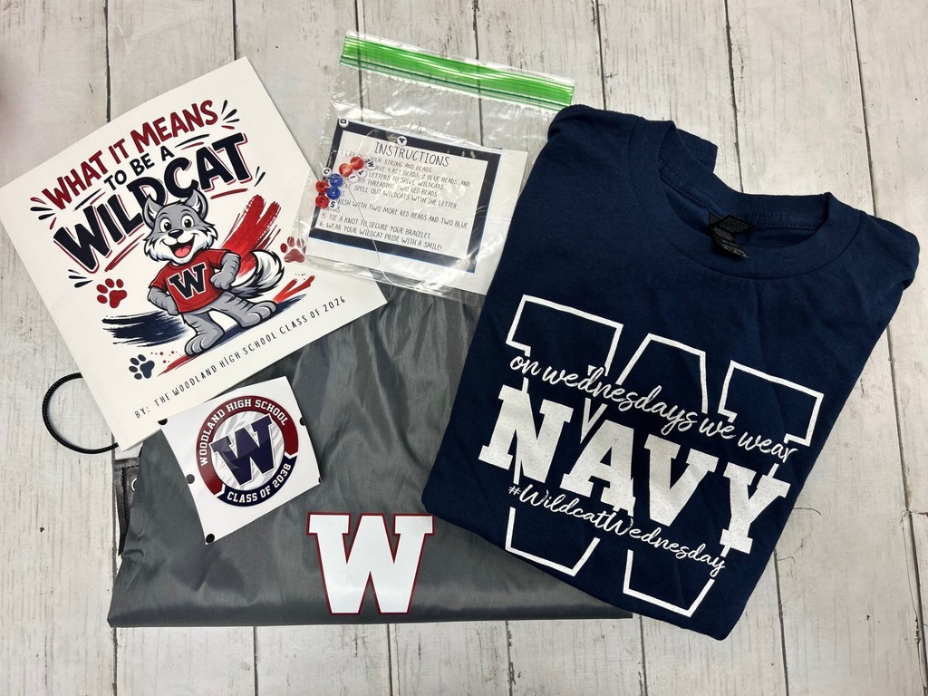 A navy blue "Navy" t-shirt, a gray bag, and a "What It Means to Be a Wildcat" book.  The t-shirt says, "On Wednesdays We Wear Navy Wildcat Wednesdays".  The grey bag has a W on it and so does the sticker with the bag.