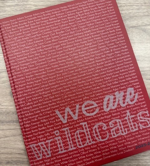 A red book with white lettering titled "We are Wildcats" placed on a wooden surface.