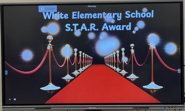 Monitor displaying a screen with a red carpet, text reading "White Elementary School S.T.A.R. Award," and decorative lights.