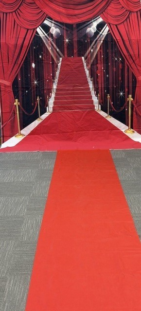 Red carpet leading to a stage with red drapes and a red background. Shiny lights are above the carpet.
