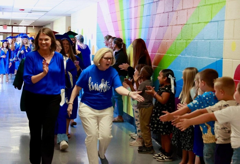 People wearing blue walk down a colorful hallway as children reach out to greet them.