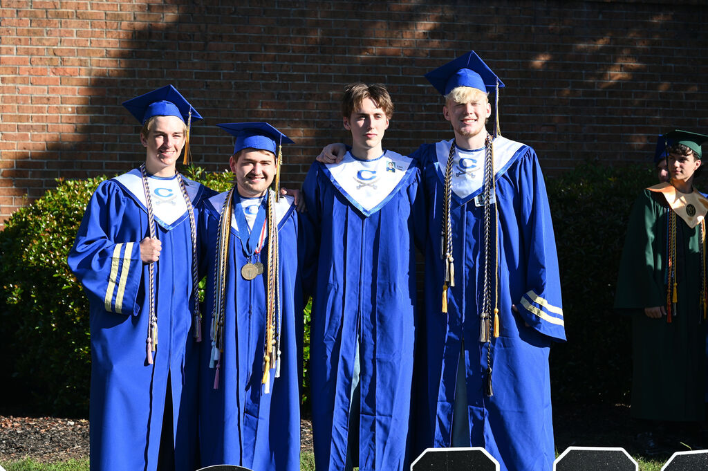 Four people in blue graduation gowns and caps, standing in front of a brick wall.