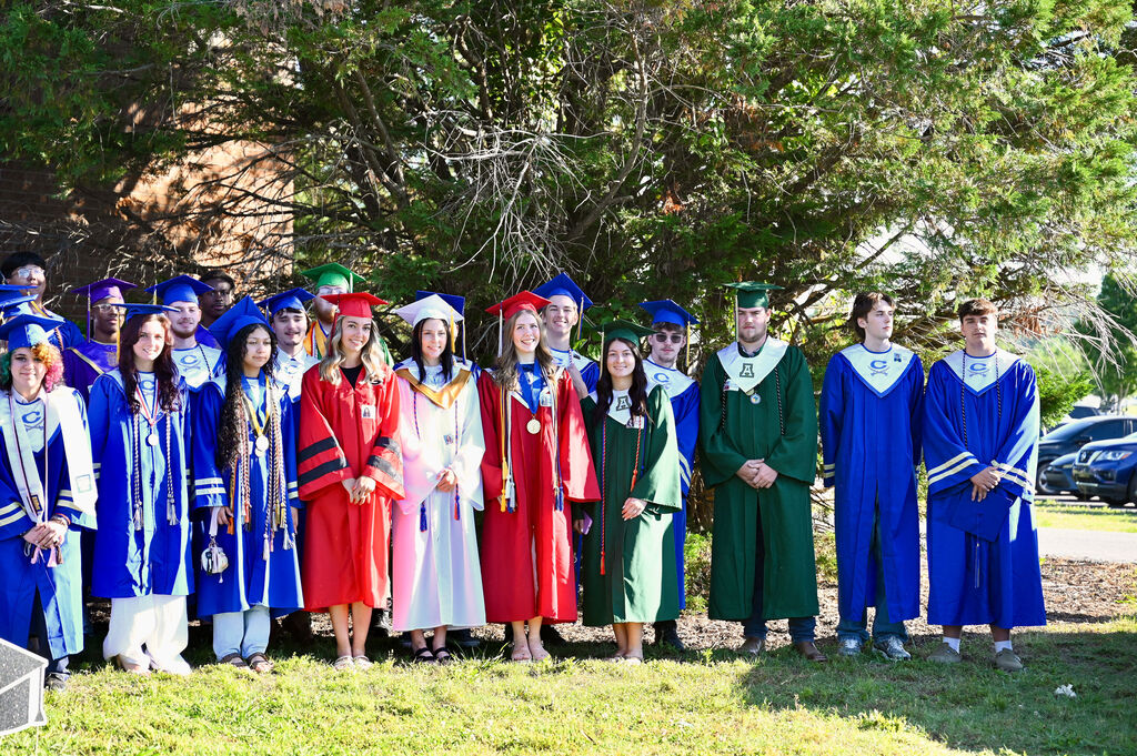 A group of people in graduation attire, including gowns and caps, posing for a photo in front of a tree.