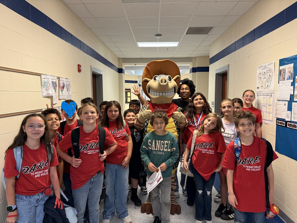 Students in red shirts, some wearing backpacks, standing in a hallway with a mascot.
