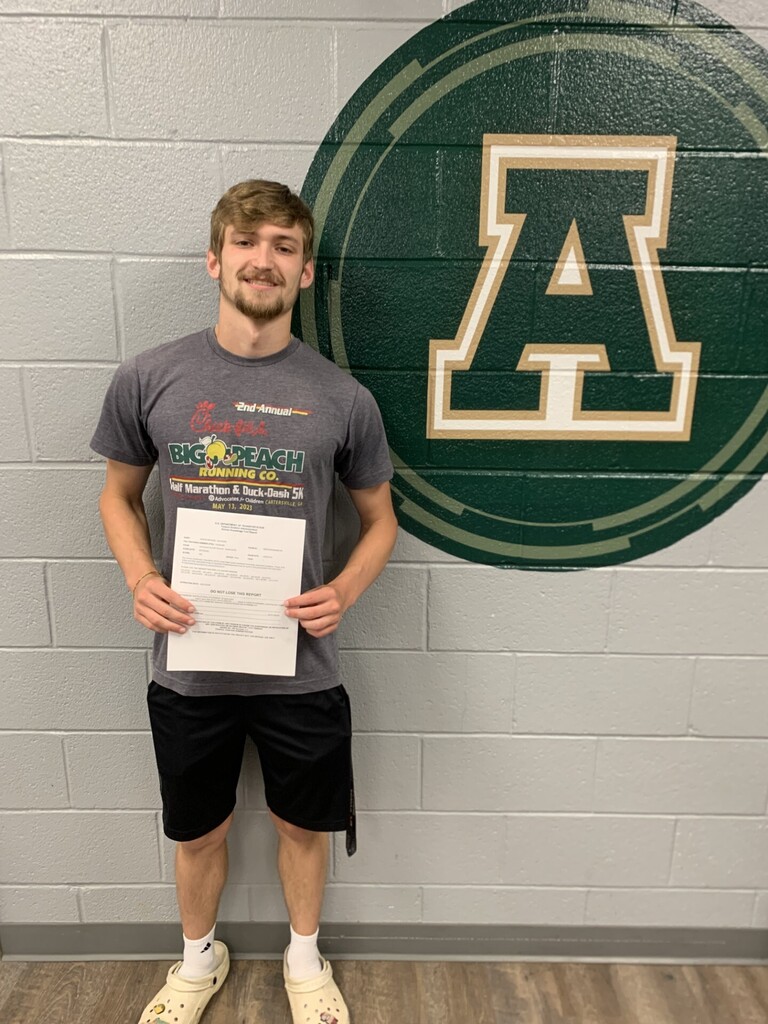 Person holds a certificate in front of a white brick wall with a green circle and the letter A.
