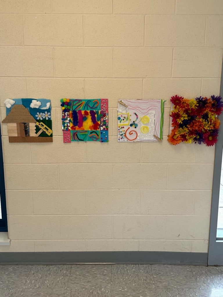 Three colorful artworks are displayed on a white wall, featuring a house, abstract patterns, and a flower arrangement.