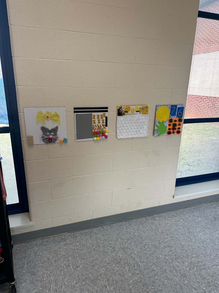 A white wall displays a cat drawing, a grid, a magnetic board, and a calendar. The room has a gray floor and windows.