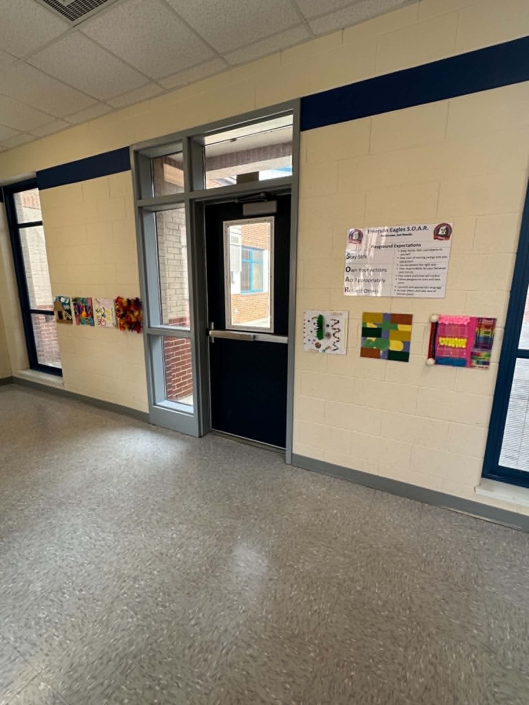 An empty room has a door, glass windows, and a bulletin board. The walls are painted light blue and white.
