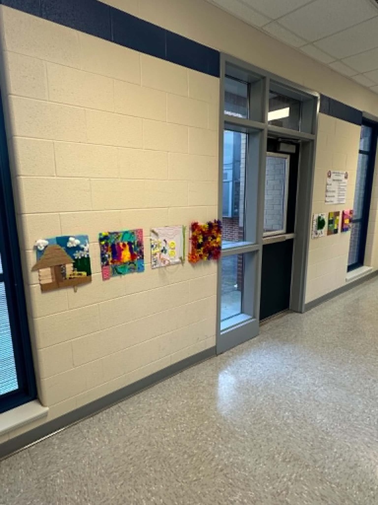 An empty hallway with white walls and blue trim. Multiple art pieces are pinned on the wall.