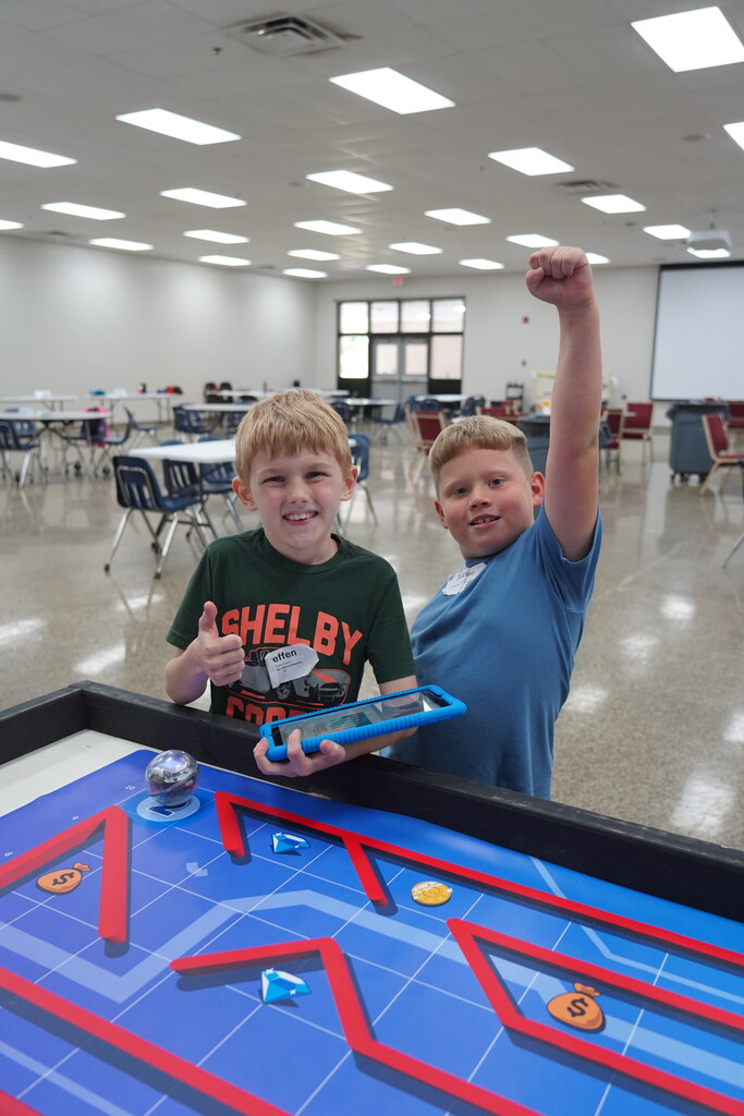 Two children playing a tabletop game with a maze and moving ball, one raising a fist.