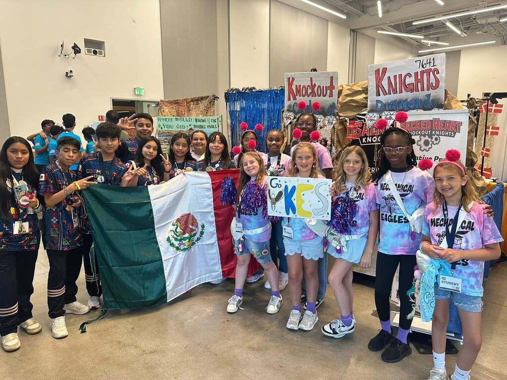 A group of individuals with a Mexican flag, banners, and holding signs inside a room.