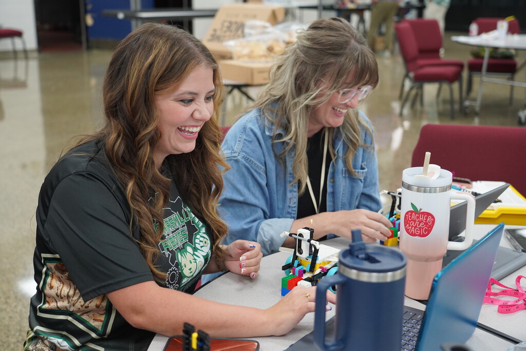 Two teachers sitting at a desk working on a robot.