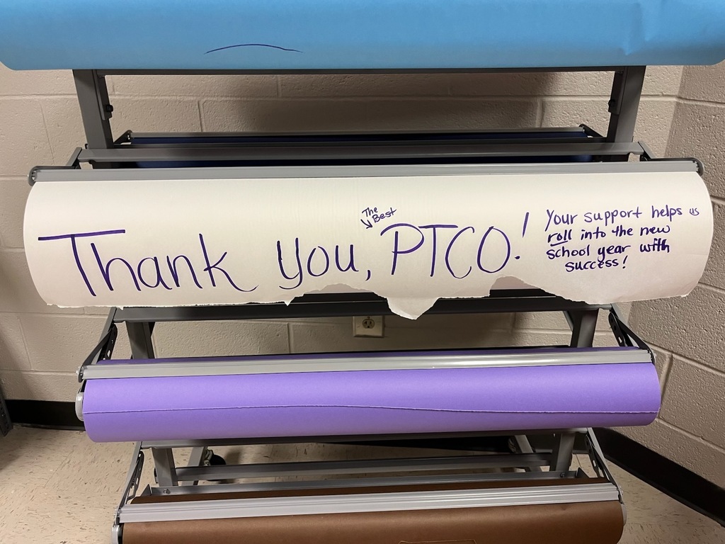 On a roll of bulletin board paper, a handwritten notes reads, "Thank You, PTCO! Your support helps us roll into the new school year with success." There are other rolls of paper on a metal stand against a plain brick wall.