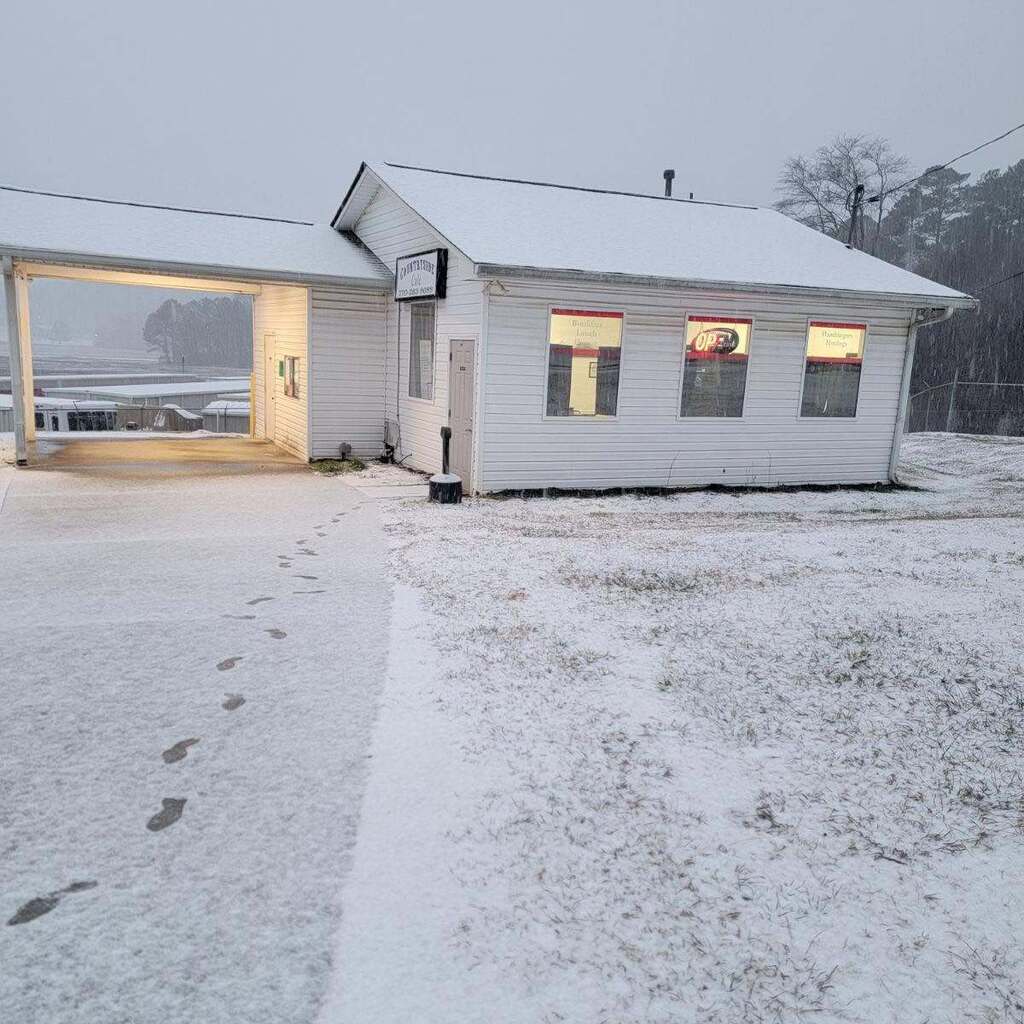 A small building with snow on the roof and windows. Footprints lead up to the front door.