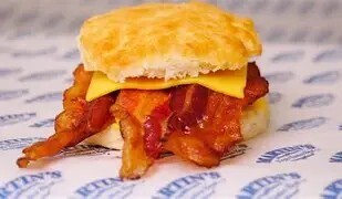 A sandwich with a biscuit, bacon, and cheese on a blue and white patterned paper.
