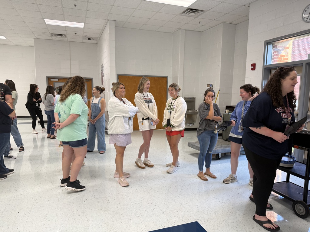 Several people stand in a room with white walls and a blue rug. A woman stands in front of a cart.