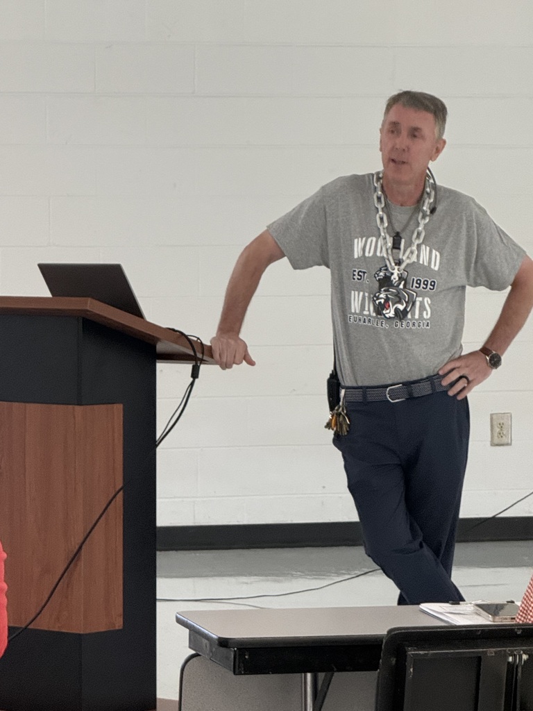 A person stands at a podium with a laptop on it, wearing a gray t-shirt and blue pants.