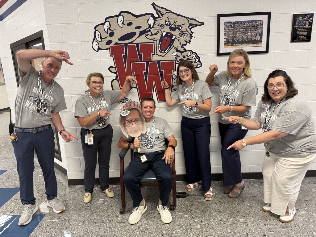 People in matching gray shirts stand around a man in a chair. They pose for a photo.