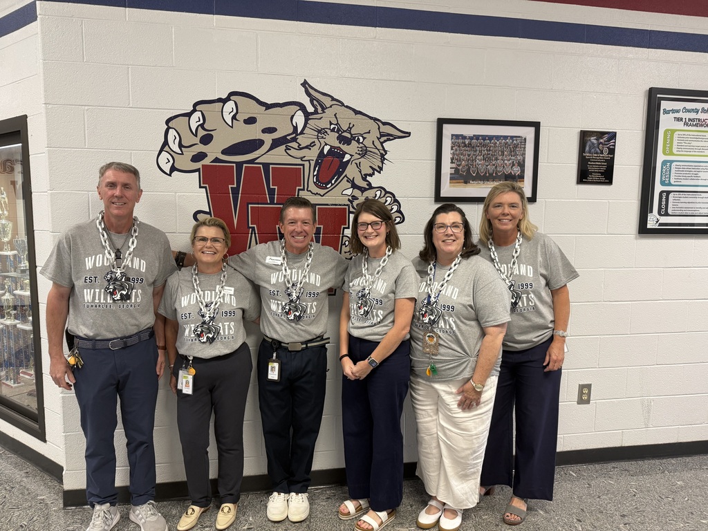 Six people in matching gray shirts and various footwear pose in front of a white wall with a logo.