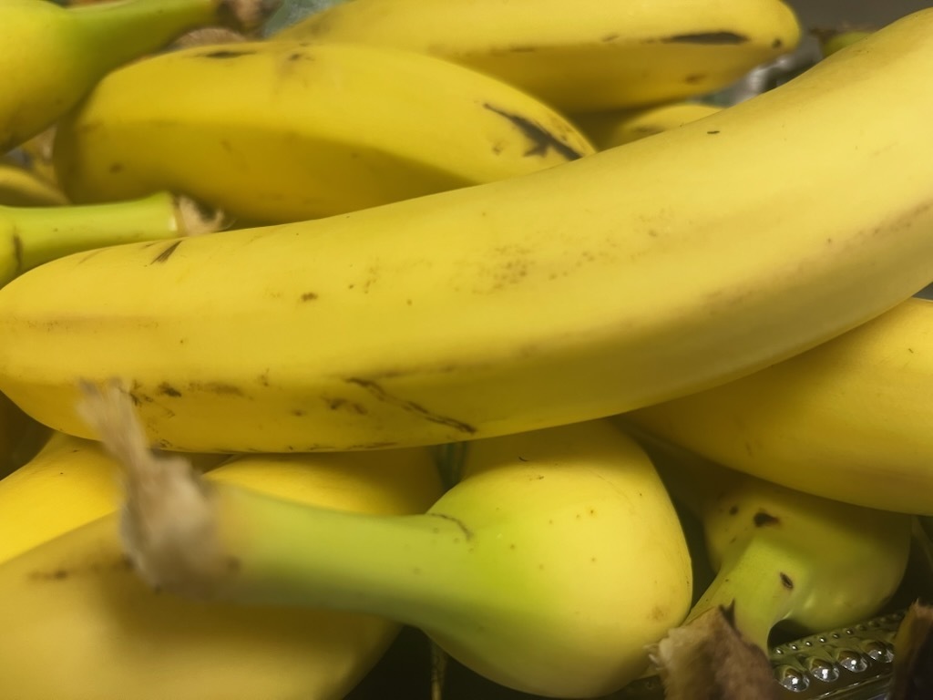 A close-up of bananas with yellow skins and green stems, some with brown spots. Some bananas are bunched together.