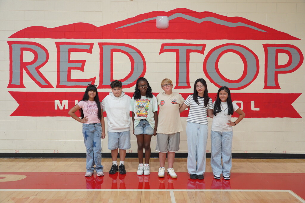 Five children standing together in front of a wall that says "Red Top" on a basketball court.