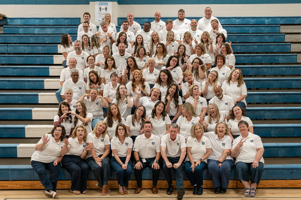A group of people in white shirts and blue pants posing for a photo on stadium bleachers.