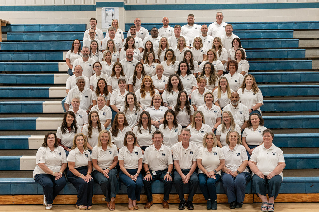Group photo of people in white shirts and jeans seated and standing on bleachers, facing the camera.