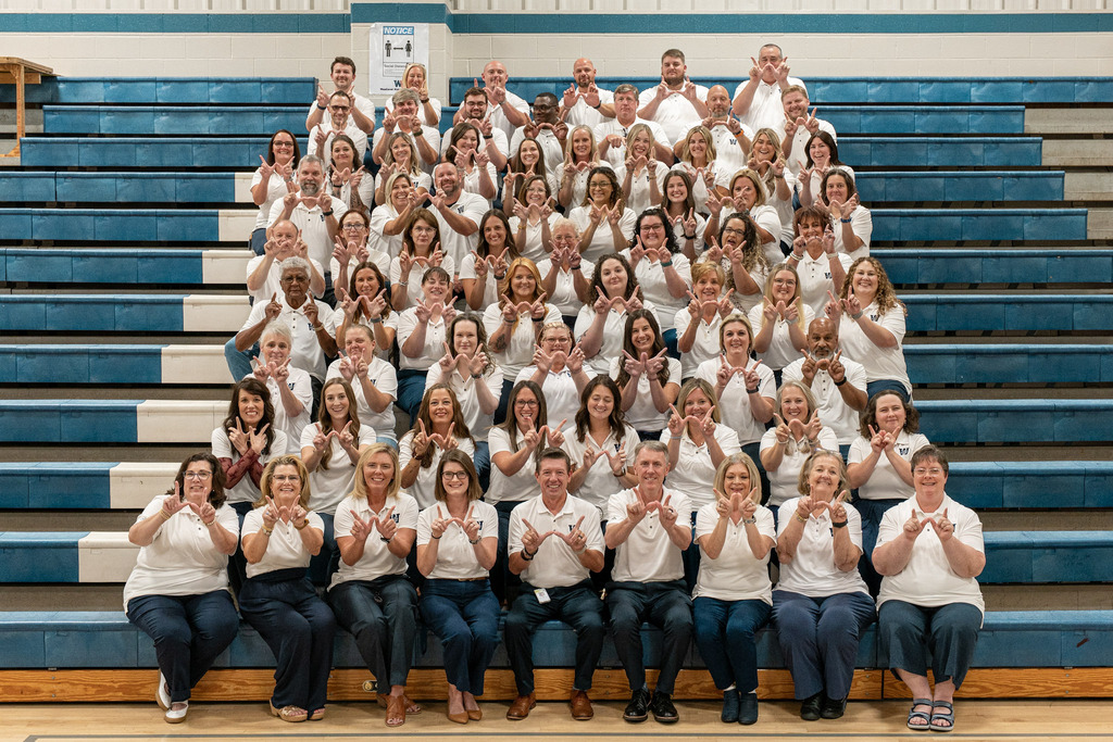 Large group of people in white shirts and jeans posing for a photo on a bleacher.
