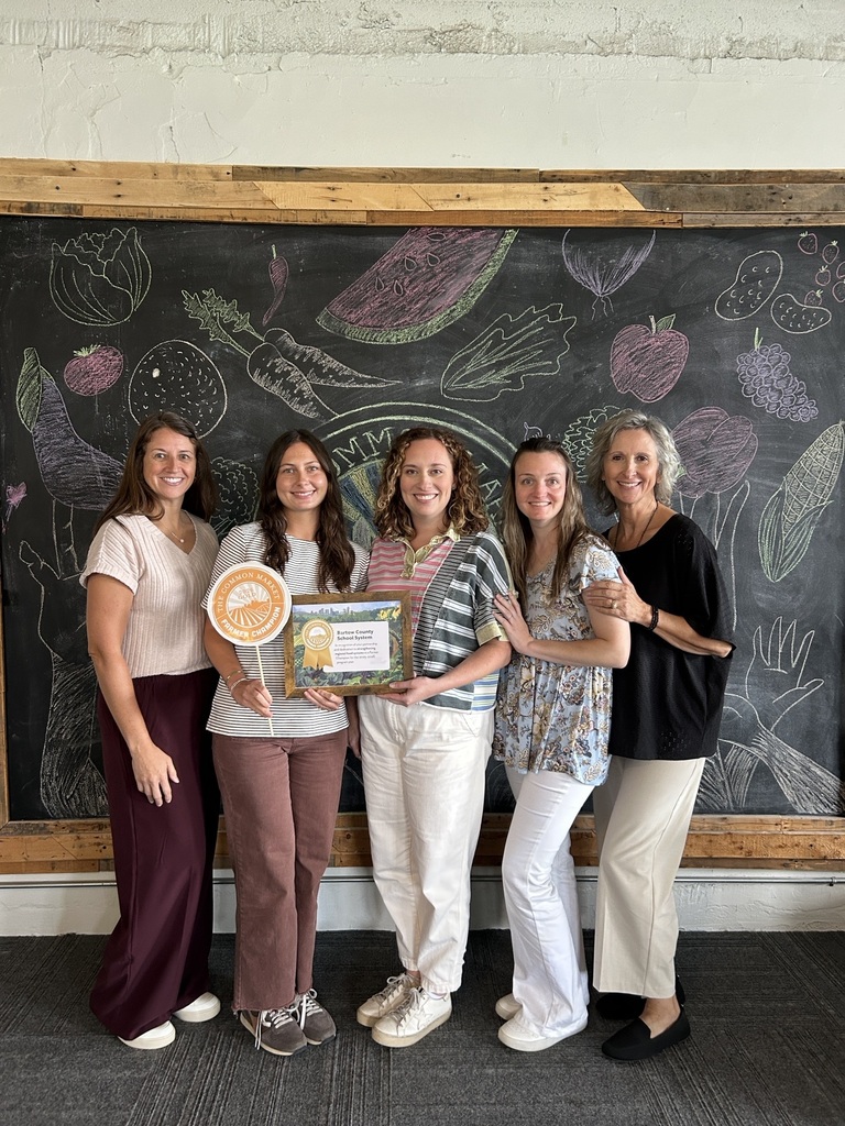 Five women stand before a chalkboard featuring drawings of fruits and vegetables, one holding a framed certificate.