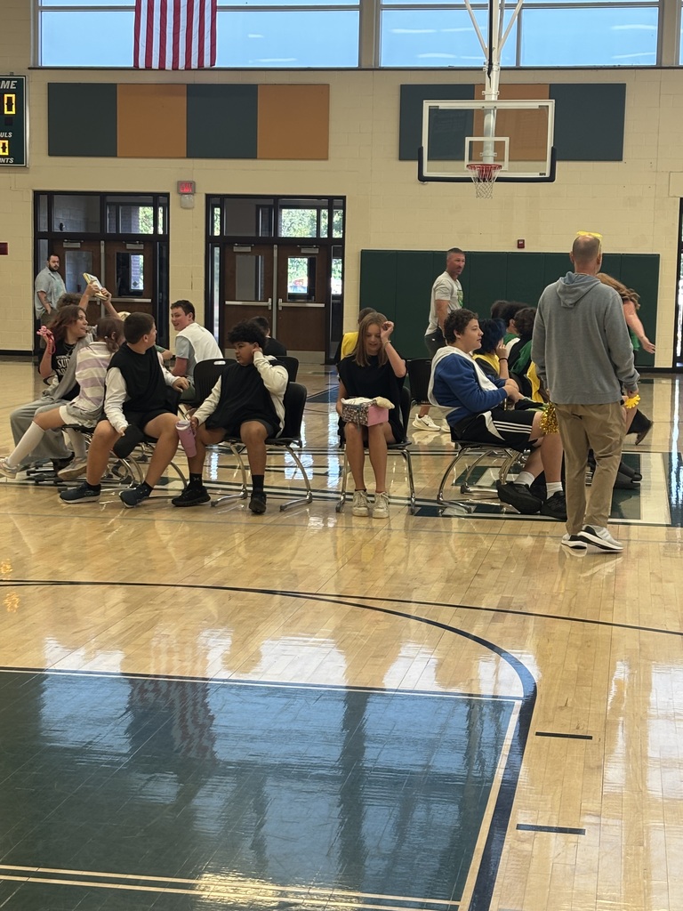 A basketball court with an American flag on the wall. People sit in chairs while others stand.