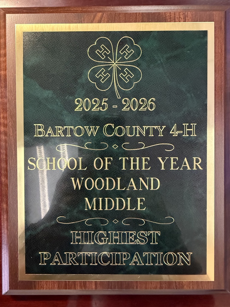 A plaque reads "2025-2026 BARTOW COUNTY 4-H SCHOOL OF THE YEAR" and "WOODLAND MIDDLE HIGHEST PARTICIPATION." The plaque has a green background and gold borders.