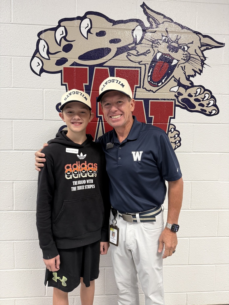 A man and a young boy stand together in front of a wall with a cat emblem.