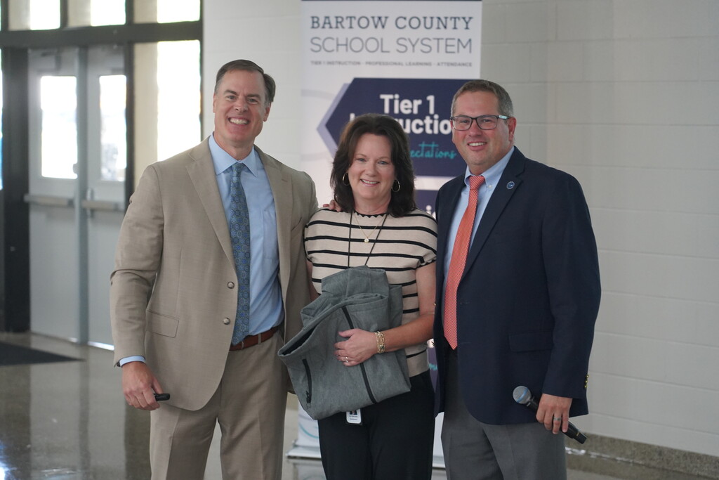 Three adults stand next to each other in front of a sign that reads "Bartow County School System".