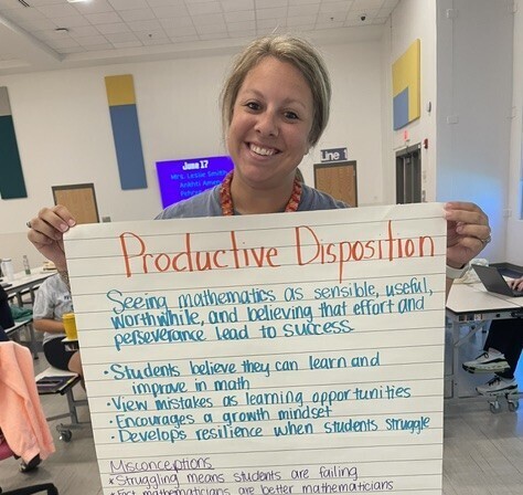 Mrs. Shields smiling for a picture and showing her groups poster for productive disposition.