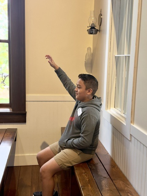 A man in a gray hoodie and khaki shorts points while sitting on a wooden bench.