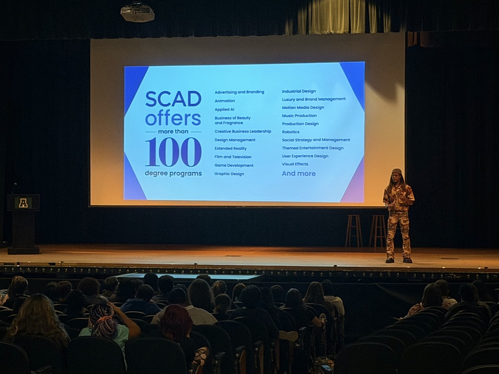 Person on stage giving a presentation on "SCAD offers 100 degree programs" to an audience.