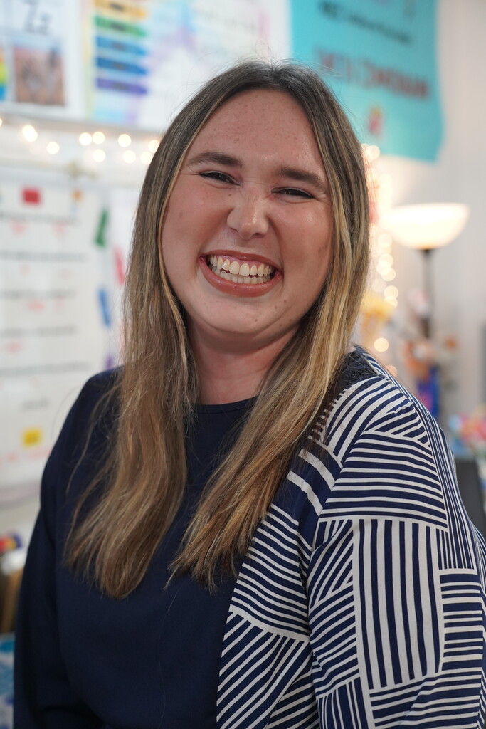 A woman with long blonde hair smiles while standing in a room with a colorful wall.