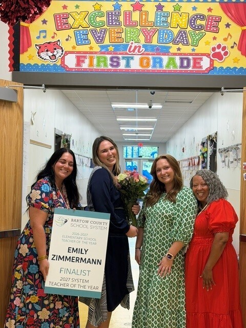 Ms. Zimmerman smiling for a picture with her grade level team and holding her Finalist sign.