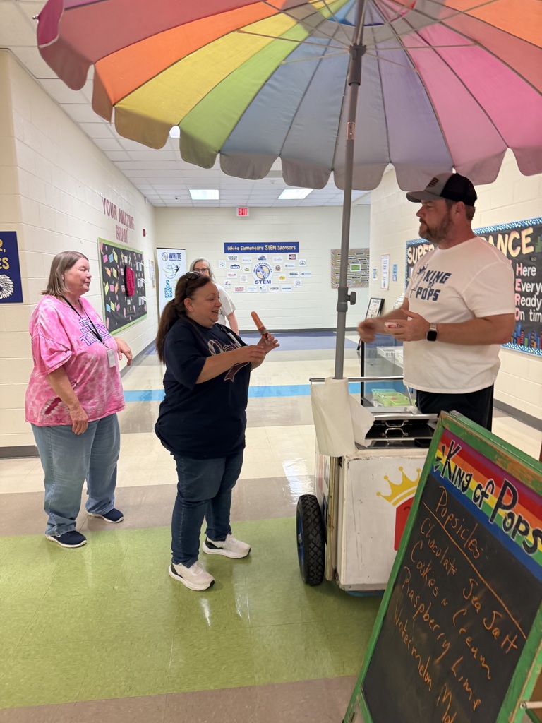 Three adults, two women and one man, stand in a hallway. A rainbow umbrella is above them.