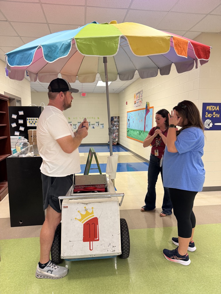 A man stands with a colorful umbrella, a cart, and two women in a hallway.