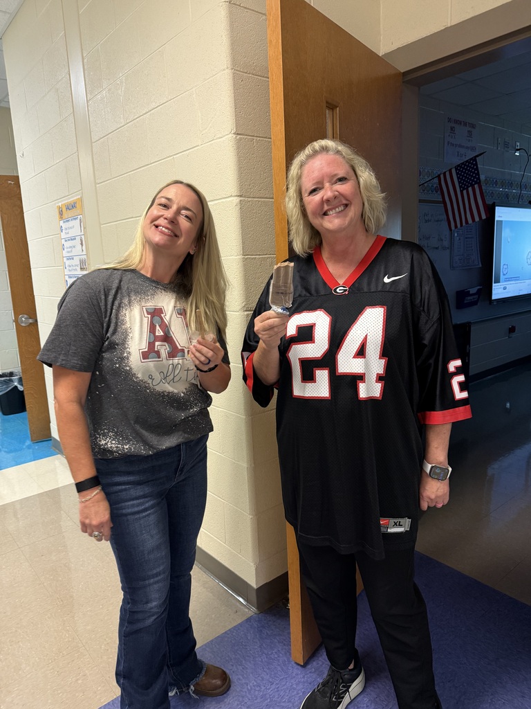Two women standing in a hallway with blue carpet, one in a gray T-shirt and the other in a football jersey.