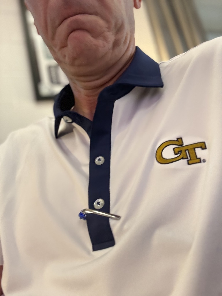 A man with a serious expression wears a white polo shirt with a blue collar and a GT logo.