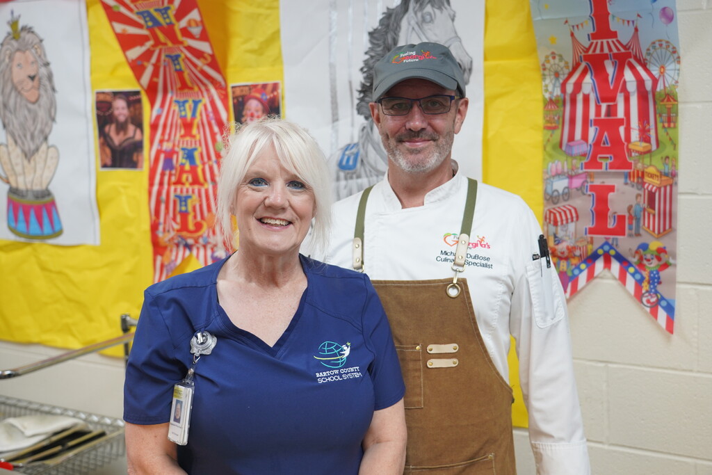 A woman in a blue shirt and a man in a white shirt and apron stand next to each other.