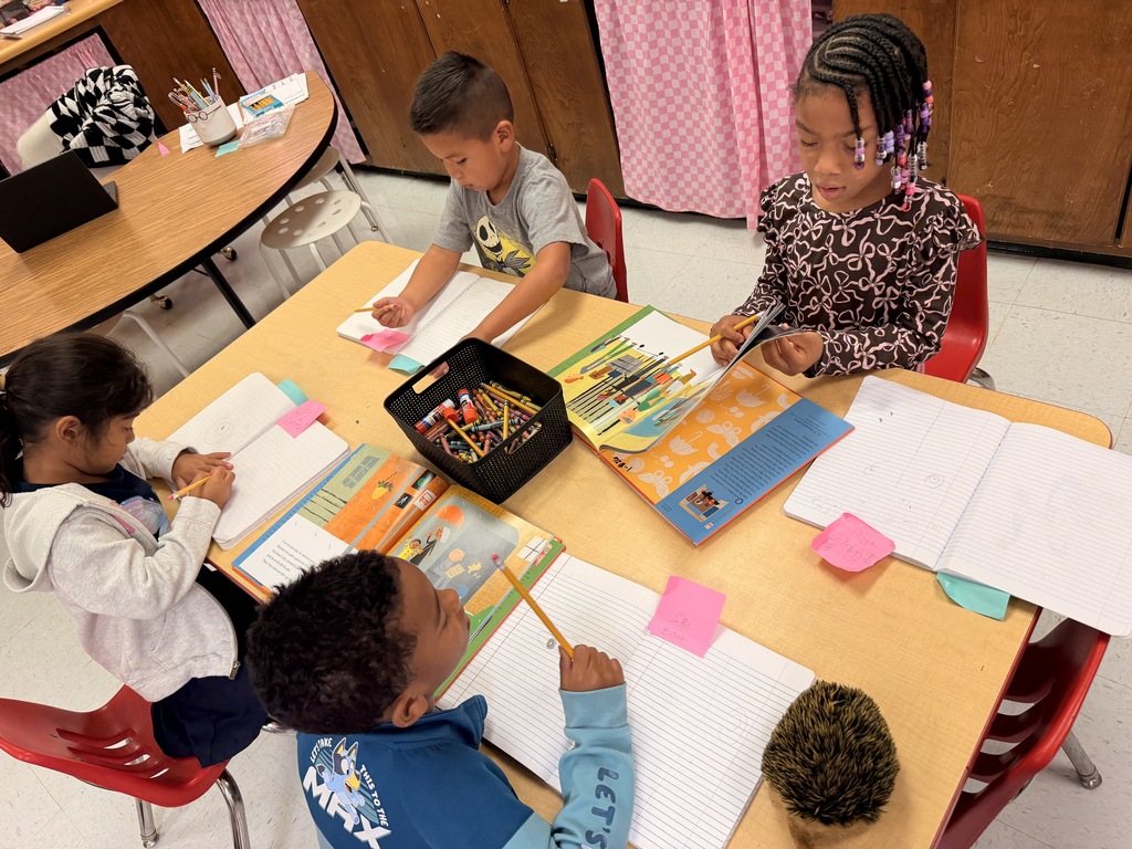 Five children sit at a table, each engaged in drawing. The table holds papers, markers, and colored pencils.
