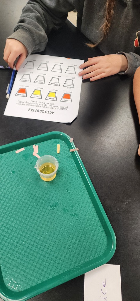 A person at a table with a green tray and small yellow liquid in a cup.