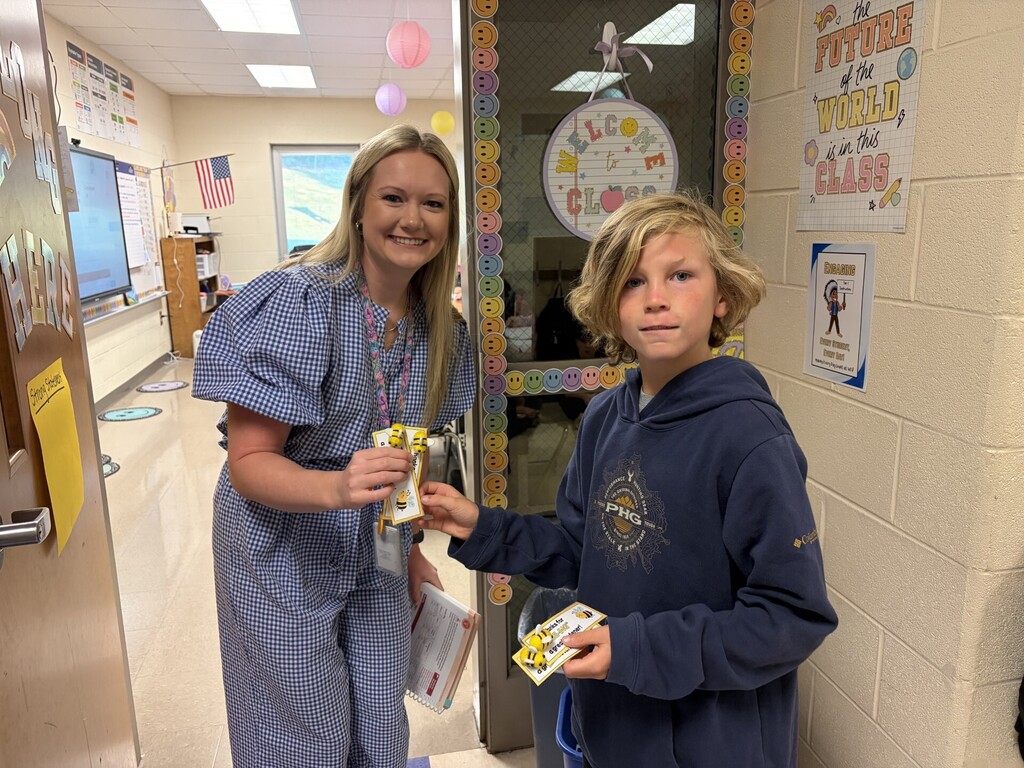 Two individuals, one in a light blue robe, the other in a navy hoodie, holding items in a school hallway.
