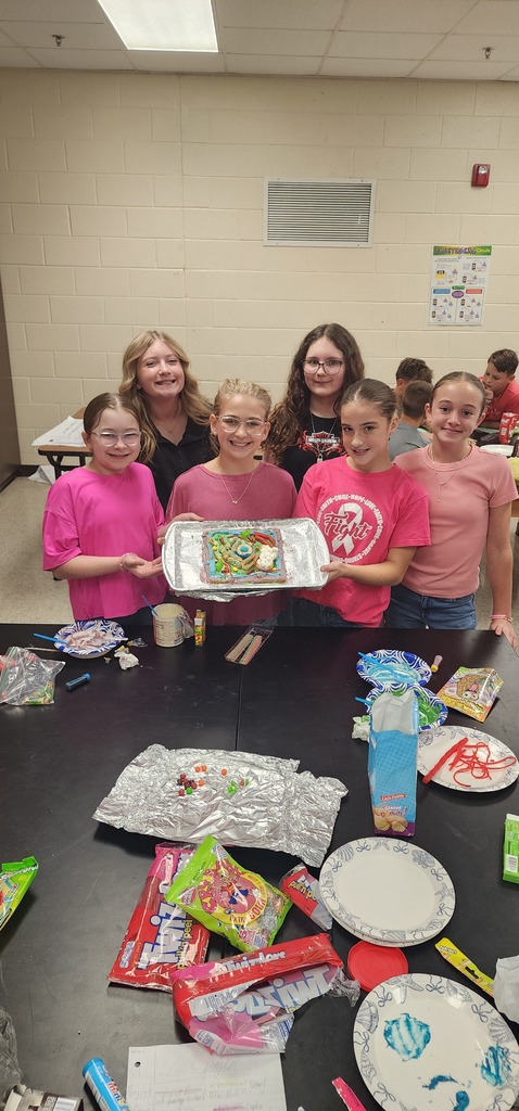 A group of girls in pink shirts hold a tray of food in a room with tables.