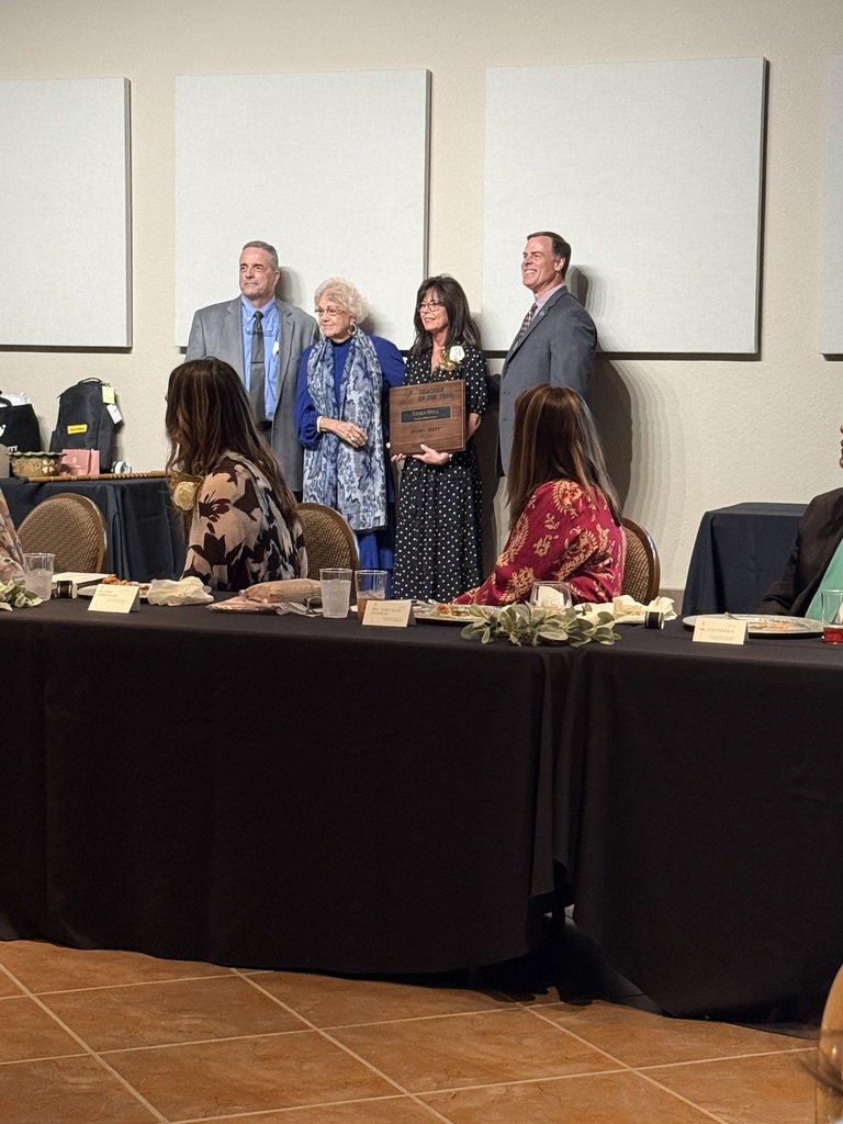 A group of people stand around a table; one holds an award. Three white boards hang on the wall behind them.