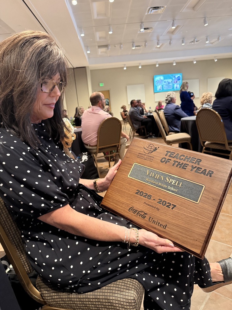 Woman holding a plaque that reads "Teacher of the Year 2018-2027" with "Pepsi United" written on it.