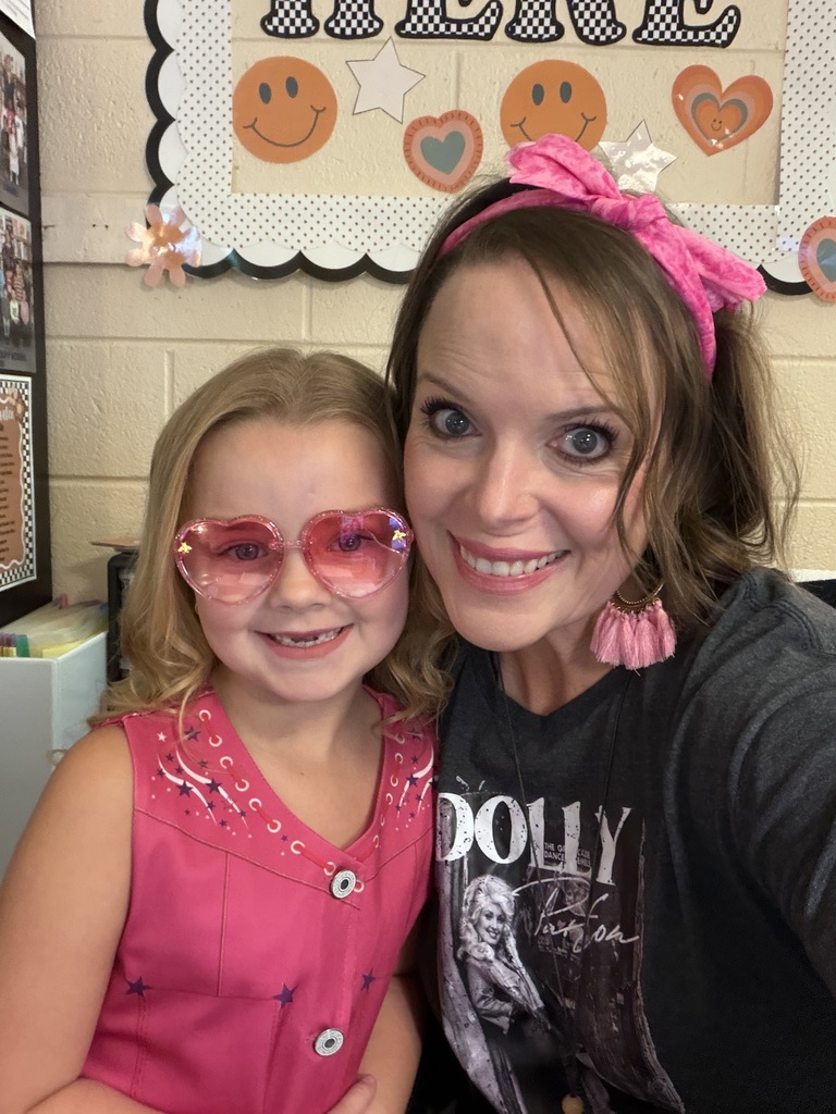 Woman and girl in front of a classroom bulletin board. Both wear pink accessories.